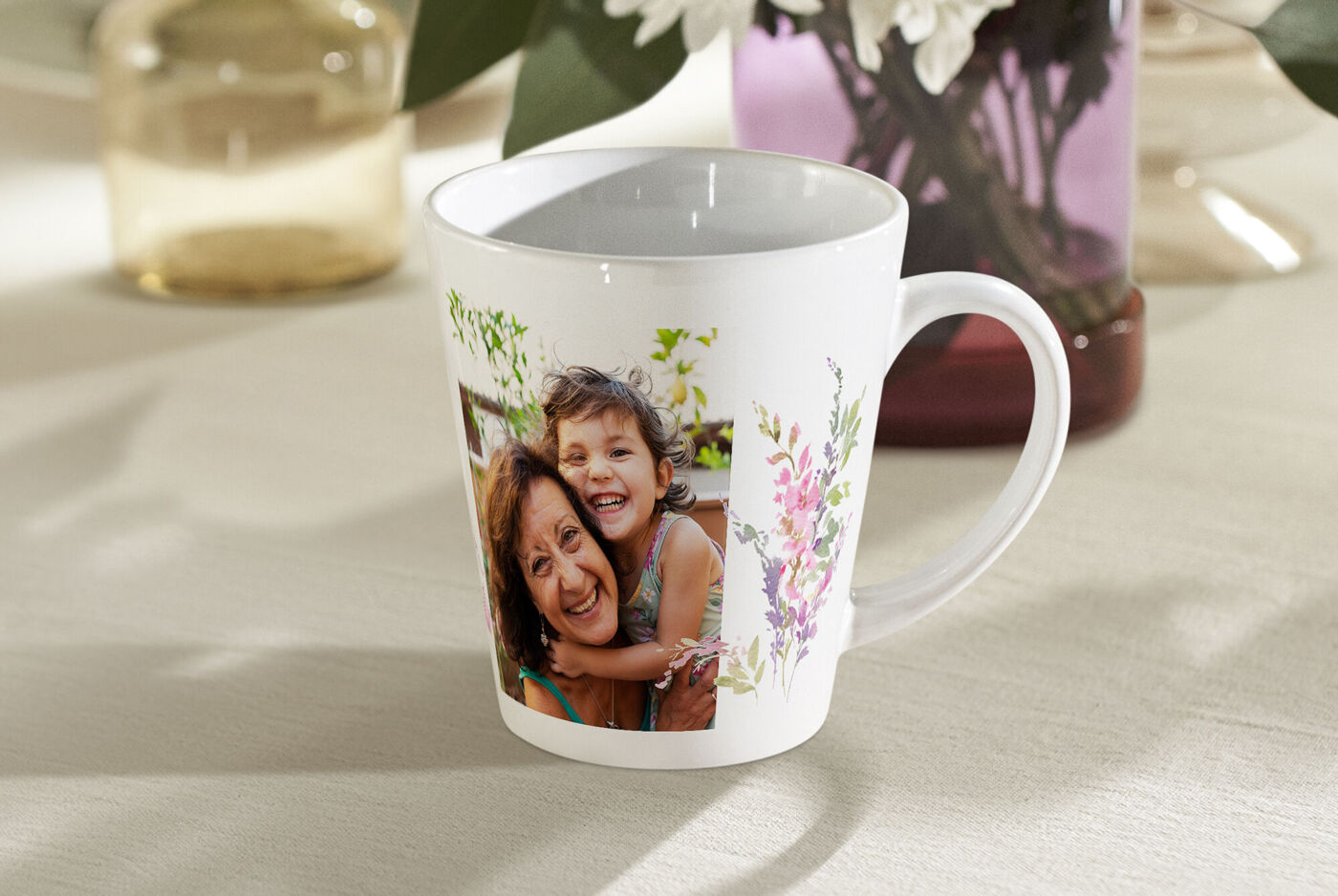 Kubek latte z uśmiechniętymi osobami i kwiatami.