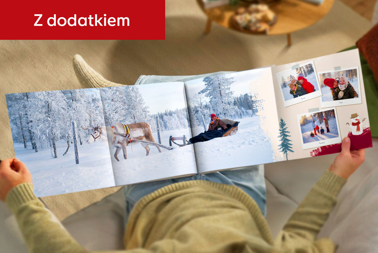Osoba trzyma rozkładaną fotoksiążkę z panoramiczną stroną: zimowy krajobraz, zaprzęg z reniferem i małe zdjęcia. Czerwony pasek Z dodatkiem