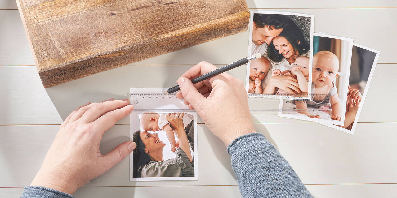 Obraz dwóch rąk wykonujących ślad na błyskawicznym zdjęciu CEWE za pomocą ołówka i linijki. Obok znajduje się drewniany klocek i trzy kolejne błyskawiczne zdjęcia.