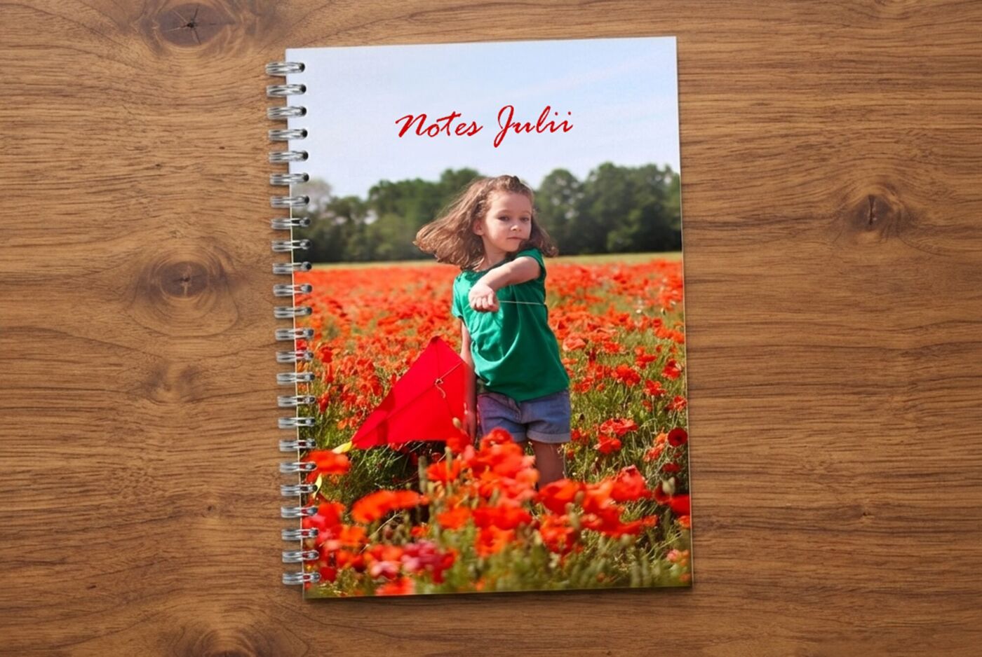 Personalizowany planer A5 z nadrukiem zdjęcia dziewczynki na polu maków i napisem "Notes Julii", leżący na drewnianym blacie.