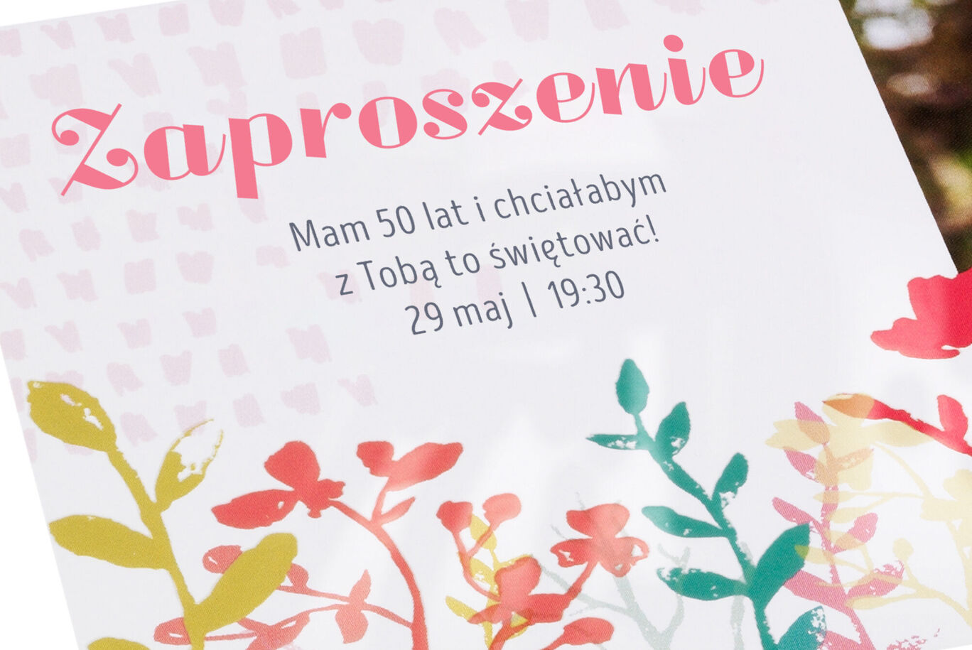 Zaproszenie z kolorowymi wzorami kwiatów i różowym tekstem.